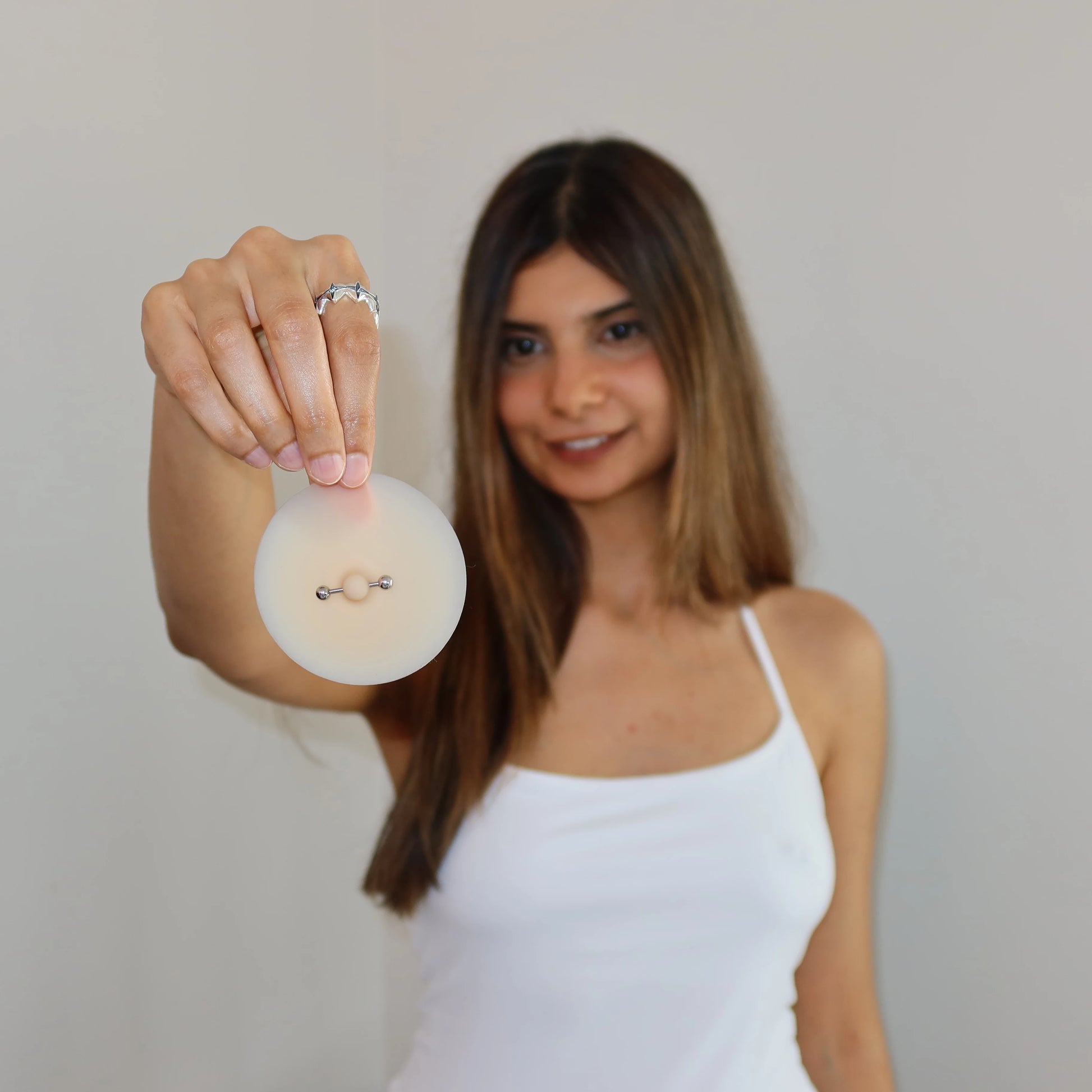 Woman holding nip stories pierced nipple covers against a plain background